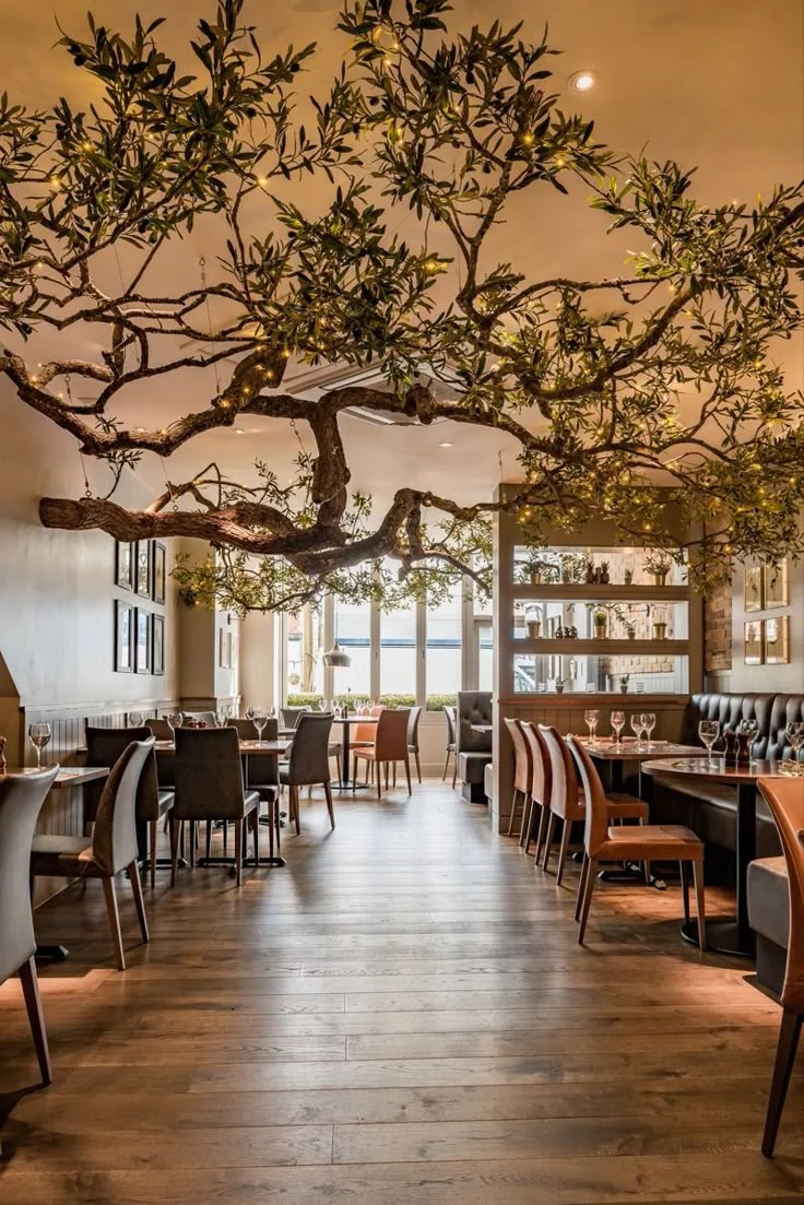 Salle de restaurant décorée d'un grand arbre dont les branches couvrent le plafond