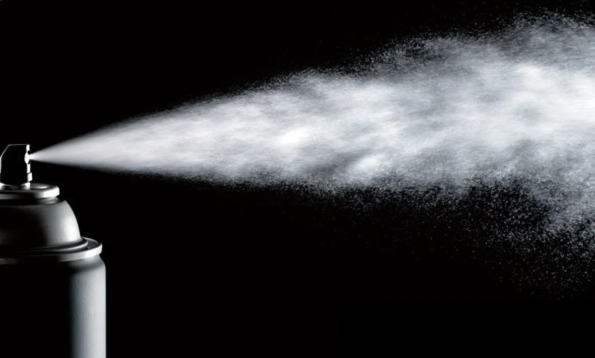 Aerosol can releasing a spray mist against a black background
