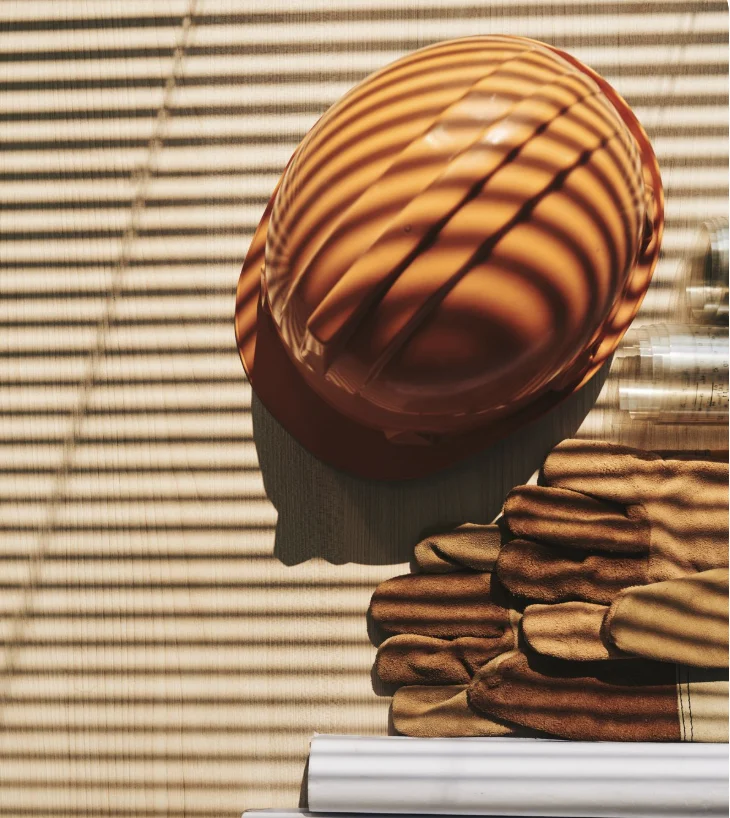 Casque de chantier orange et gants de travail, rayés par l'ombre d'un store