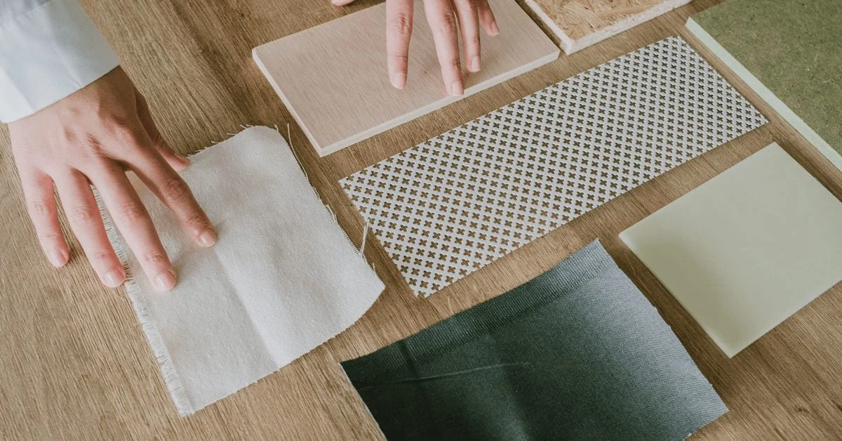 Hands arranging fabric and material samples on a wooden table