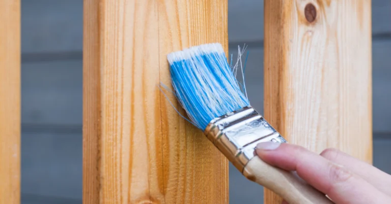 Main appliquant un vernis au pinceau sur une planche de bois